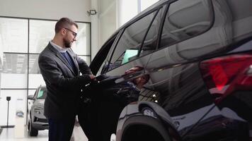 un elegante hombre en lentes y traje examinar vehículo antes de haciendo compra. comprar coche video