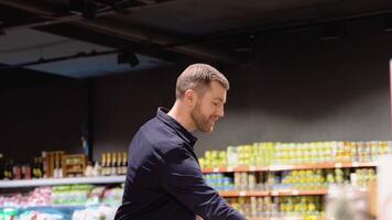 jong Mens kiezen aubergine Bij supermarkt. kiezen voedsel van plank in supermarkt video