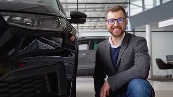 portret van een jong Mens in bril en pak in de buurt een nieuw auto in een auto handel video