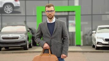 Business, confident stylish man stands with a bag near a car dealership before buying a new car video