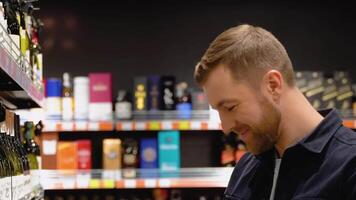 un hombre toma alcohólico bebidas desde el supermercado estante. compras para alcohol en el Tienda video