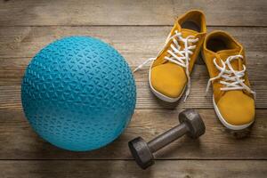 heavy rubber slam ball filled with sand, iron dumbbell and minimalist barefoot sneakers on a rustic wooden deck, exercise and fitness concept photo