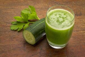 glass of fresh green vegetable juice with cucumber and celery leaf against grunge wood photo