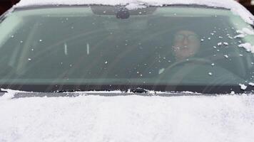 Young man cleaning snow from car windshield outdoors on winter day video