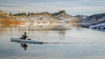 senior male wearing life jacket is paddling expedition canoe in winter scenery of Horsetooth Reservoir in northern Colorado photo