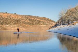 male paddler in red drysuit is paddling a stand up paddleboard on mountain lake in Colorado, winter scenery photo