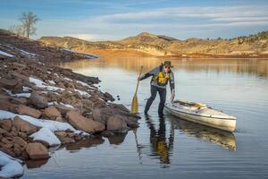 senior male wearing life jacket is paddling expedition canoe in winter scenery of Horsetooth Reservoir in northern Colorado photo