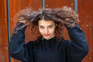 blanco morena Adolescente niña con Rizado pelo poses en el calle en el ciudad. foto