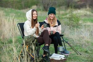 Two young women hiking in the mountains and drinking tea from a kettle. Travel, traveler. photo