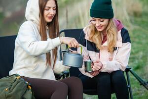 Two young women hiking in the mountains and drinking tea from a kettle. Travel, traveler. photo