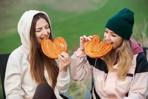 Two young women in warm clothes having fun and eating cookies in the park photo