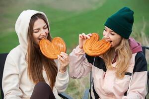 dos joven mujer en calentar ropa teniendo divertido y comiendo galletas en el parque foto