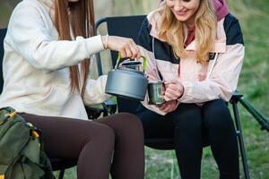 Two young women hiking in the mountains and drinking tea from a kettle. Travel, traveler. photo