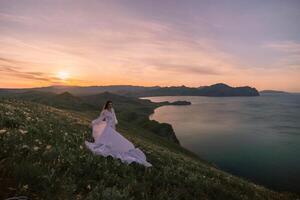 A woman in a white dress is standing on a hill overlooking a body of water photo