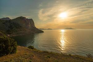 A beautiful sunset over the ocean with a mountain in the background. The sky is filled with clouds and the sun is setting. The water is calm and the sky is a mix of orange and pink hues. photo