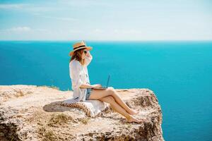 Freelance woman working on a laptop by the sea, typing away on the keyboard while enjoying the beautiful view, highlighting the idea of remote work. photo