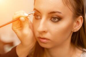 Make-up artist paints eyebrow pencil to beautiful brunette in be photo