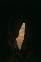 A cave with a small opening in the wall. The cave is dark and the sky is cloudy. photo