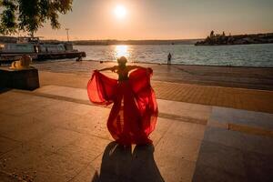 amanecer rojo vestido. un mujer en un largo rojo vestir en contra el fondo de amanecer, brillante dorado ligero de el del sol rayos el concepto de feminidad, armonía. foto