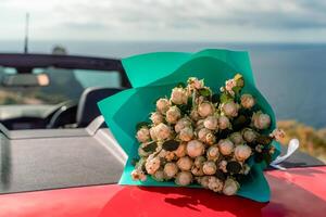A bouquet of flowers is sitting on the hood of a red car. The flowers are white and red, and they are arranged in a vase. Concept of romance and love. photo