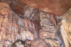 un cueva con un lote de rock formaciones y estalactitas colgando desde el techo. escena es misterioso y temor inspirador. foto