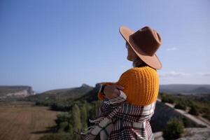 A woman wearing a brown hat and a yellow sweater is standing on a hillside photo