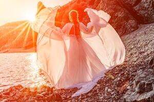 misterioso mujer silueta largo pelo camina en el playa Oceano agua, mar ninfa viento escucha a el ola. lanza arriba un largo blanco vestido, un adivinar puesta de sol. artístico foto desde el espalda sin un cara