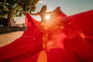 amanecer rojo vestido. un mujer en un largo rojo vestir en contra el fondo de amanecer, brillante dorado ligero de el del sol rayos el concepto de feminidad, armonía. foto