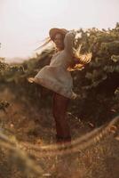 Woman with straw hat stands in front of vineyard. She is wearing a light dress and posing for a photo. Travel concept to different countries photo