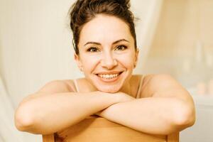 retrato de un de edad mediana mujer, sonriente con su brazos doblada en frente de su rostro, su pelo tirado arriba. el morena es en un bueno humor. en un ligero antecedentes. foto