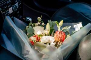 A bouquet of flowers is sitting in a car. The flowers are white and red, and they are in a clear plastic bag. photo