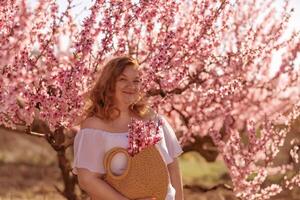 Woman blooming peach orchard. Against the backdrop of a picturesque peach orchard, a woman in a long white dress and hat enjoys a peaceful walk in the park, surrounded by the beauty of nature. photo