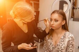 Make-up artist paints eyebrow pencil to beautiful brunette in be photo