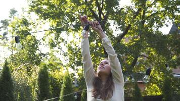 Woman decorator prepares black wire garland bulbs for wedding ceremonies in garden. Female designer preparing outdoor light for wedding ceremony. Decoration with flowers and lamps in wedding arch. video