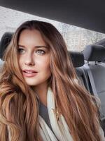 Young woman with long hair, wavy hairstyle in the car or taxi cab as passenger, exploring the city, transport and travel photo