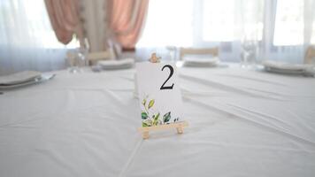 mesa número en restaurante servido con vajilla es preparado para festivo evento sin personas y alimento. Boda mesa decorado. invitado mesa número. Boda mesa en el restaurante. boda. banquete. video