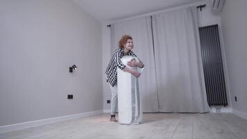 Mature woman unpacking new bed mattress while moving into new apartment. Happy elderly woman unpacking new orthopedic mattress in an empty living room. Furnishing new house. Renting a house. video