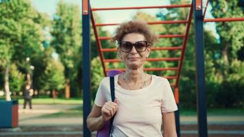 Happy senior woman going on sport training, carry yoga mat. Health and sport. Joyful mature female with mat going practice yoga exercises outdoors. Elderly sportswoman carrying rolled mat for fitness. video