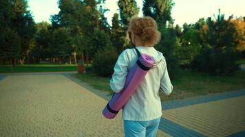 Senior woman with fitness mat walking. Happy mature lady going at outdoors yoga class. Active lifestyle. Restart of normal life after pandemic. Elderly woman walking with exercise mat on workout. video