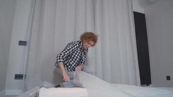 Mature woman unpacking new bed mattress while moving into new apartment. Happy elderly woman unpacking new orthopedic mattress in an empty living room. Furnishing new house. Renting a house. video