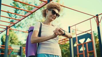 glücklich Alten Frau im gut physisch gestalten Verwendet Fitness Tracker nach Yoga Klasse außen. modern Sport Geräte, das Konzept von Fitness Ausrüstung. Sport Clever betrachten. gesund Lebensstil auf Ruhestand. video