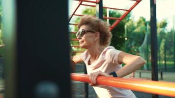 Senior woman working strength training push ups outdoor. Mature athletic skinny female doing arm exercises push-ups from the bar at the outdoor gym in the summer. A healthy way of life for the elderly video