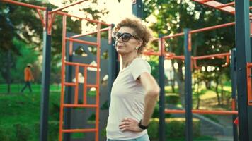 Mature woman warming up before workout at outdoor gym in summer. Elderly female doing exercises to warm up arms and upper shoulder zone at the street fitness area. Healthy lifestyle in retirement. video