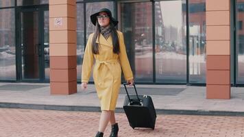 stylish girl with long hair in a hat and glasses comes with luggage. slow motion video