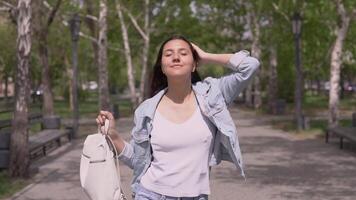 funny girl in a good mood with long hair in a denim jacket and a backpack walking down the street in sunny weather and dancing funny. slow motion video