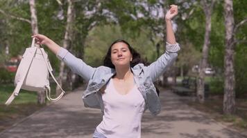 rolig flicka med lång hår i en denim jacka och en ryggsäck promenader ner de gata och danser rolig.långsam rörelse video