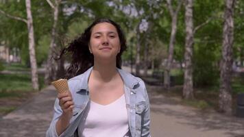 uma lindo jovem menina anda em baixa a rua e come gelo creme em uma quente verão dia.lento movimento video