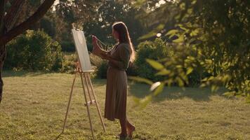 Creative woman artist paints a picture with a brush while standing near the easel in nature. Woman Artist, Art for Sales, Inspiration in Nature. video