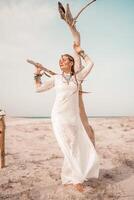 modelo en boho estilo en un blanco largo vestir y plata joyería en el playa. su pelo es trenzado, y allí son muchos esposas en su brazos. foto