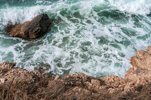 The ocean is rough and the waves are crashing against the rocks. The water is a deep blue color and the rocks are grey. photo